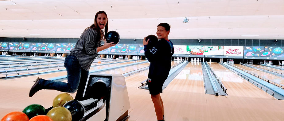 woman and child holding bowling balls in front of the bowling alley