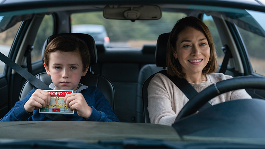 Mother sitting in the car with her 11 year old son. He's holding a fake monopoly card.