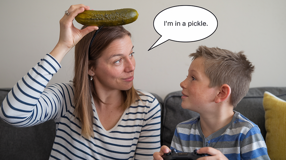 The image shows a woman holding a pickle on top of her head while looking at a boy. The boy is holding a game controller, and they are both smiling. The woman has a speech bubble that says, "I'm in a pickle."